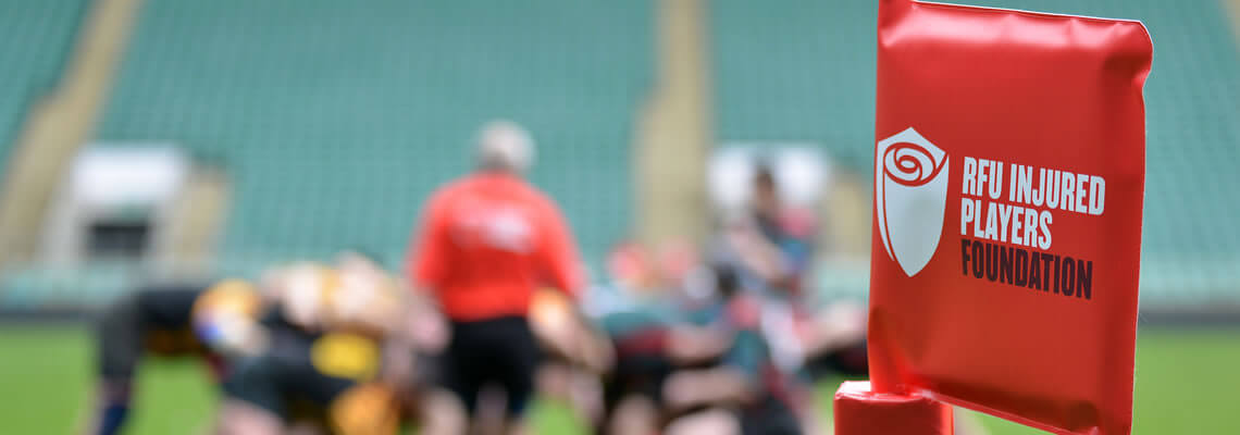 Red corner flag with IPF logo. Out of focus behind it is a rugby scrum.